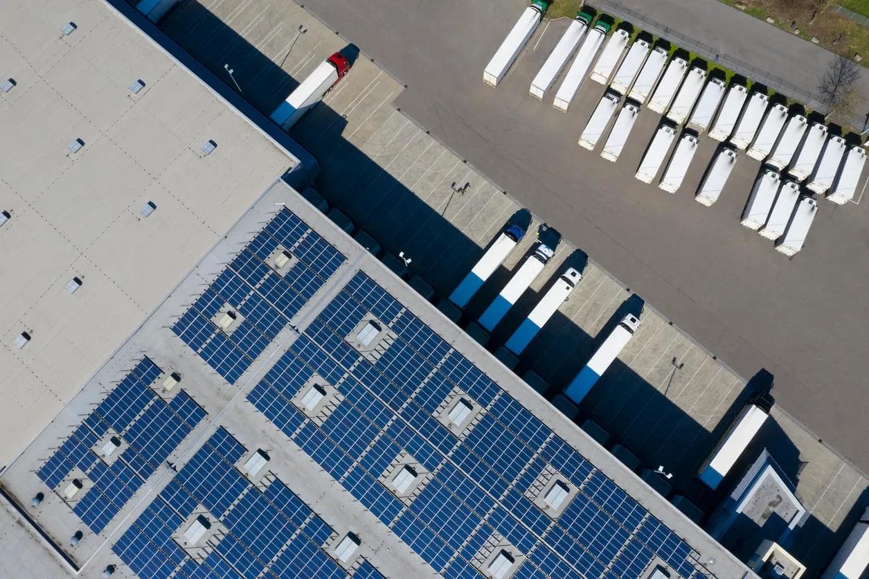 Aerial view of trucks during unloading and a large storehouse with solar panels on the rooftop. 