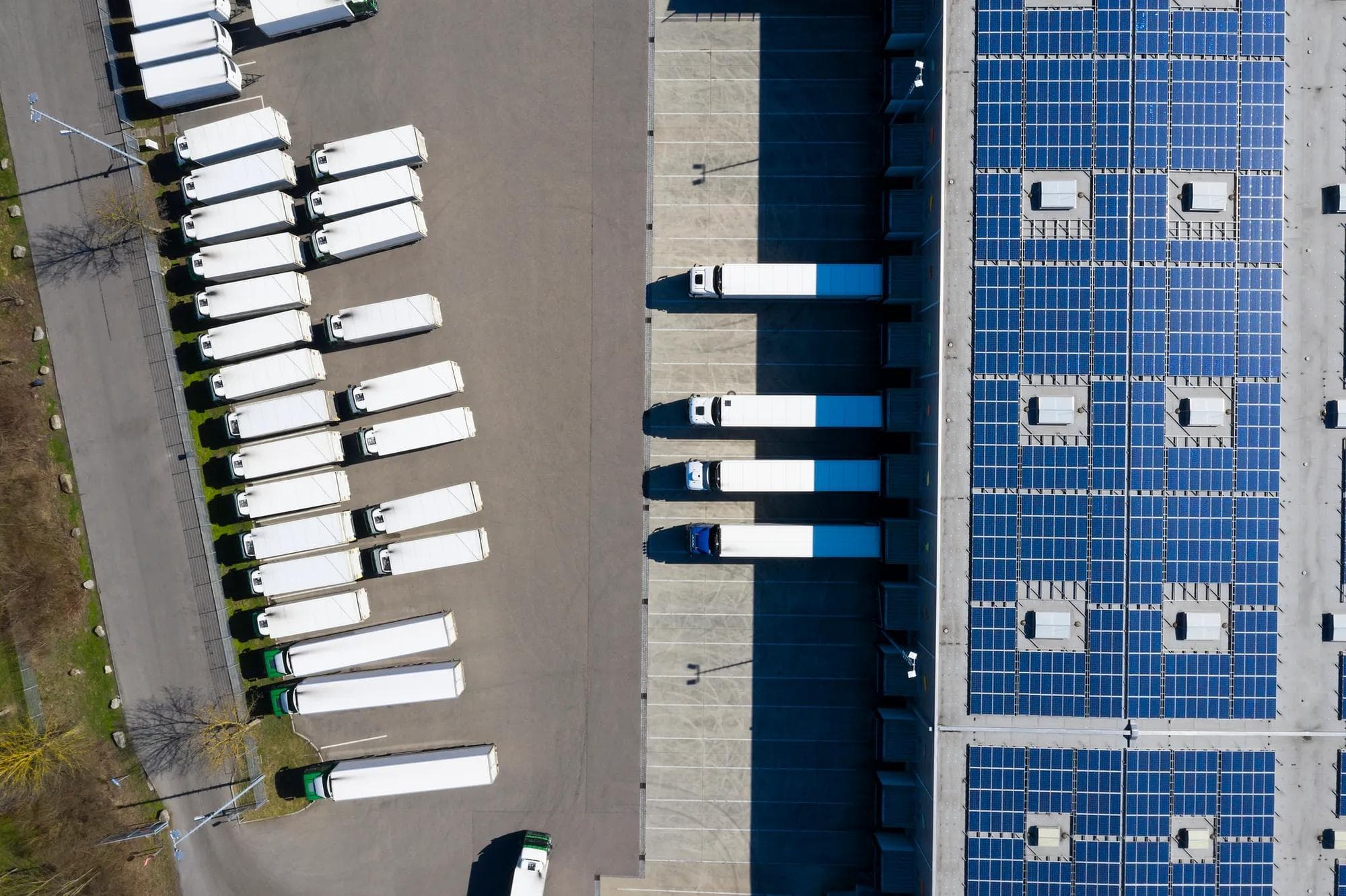 Aerial view of trucks during unloading and a large storehouse with solar panels on the rooftop.