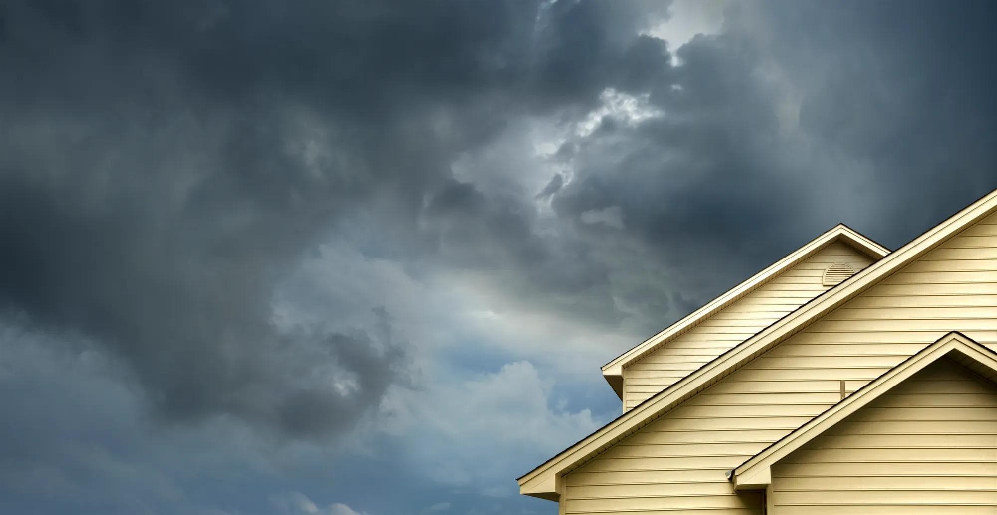 A building with yellow siding and storm clouds. 