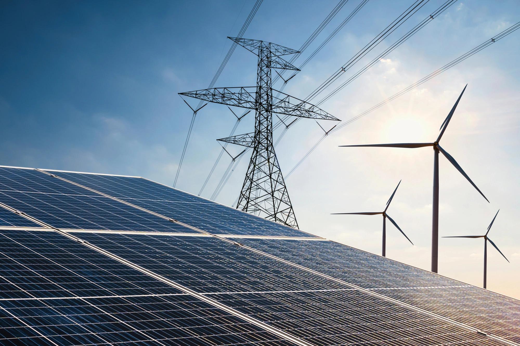 Solar panels and wind turbines with a transmission tower in the background.  