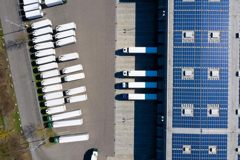 Aerial view of trucks during unloading and a large storehouse with solar panels on the rooftop.
