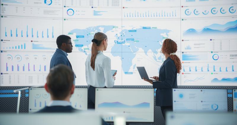 A diverse team discusses global risks in front of a digital map of the world.
