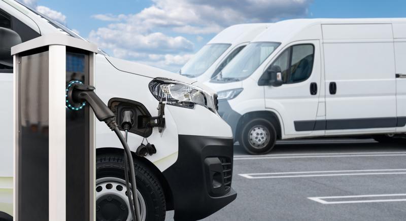 Electric delivery van with other electric vehicles at a charging station. 