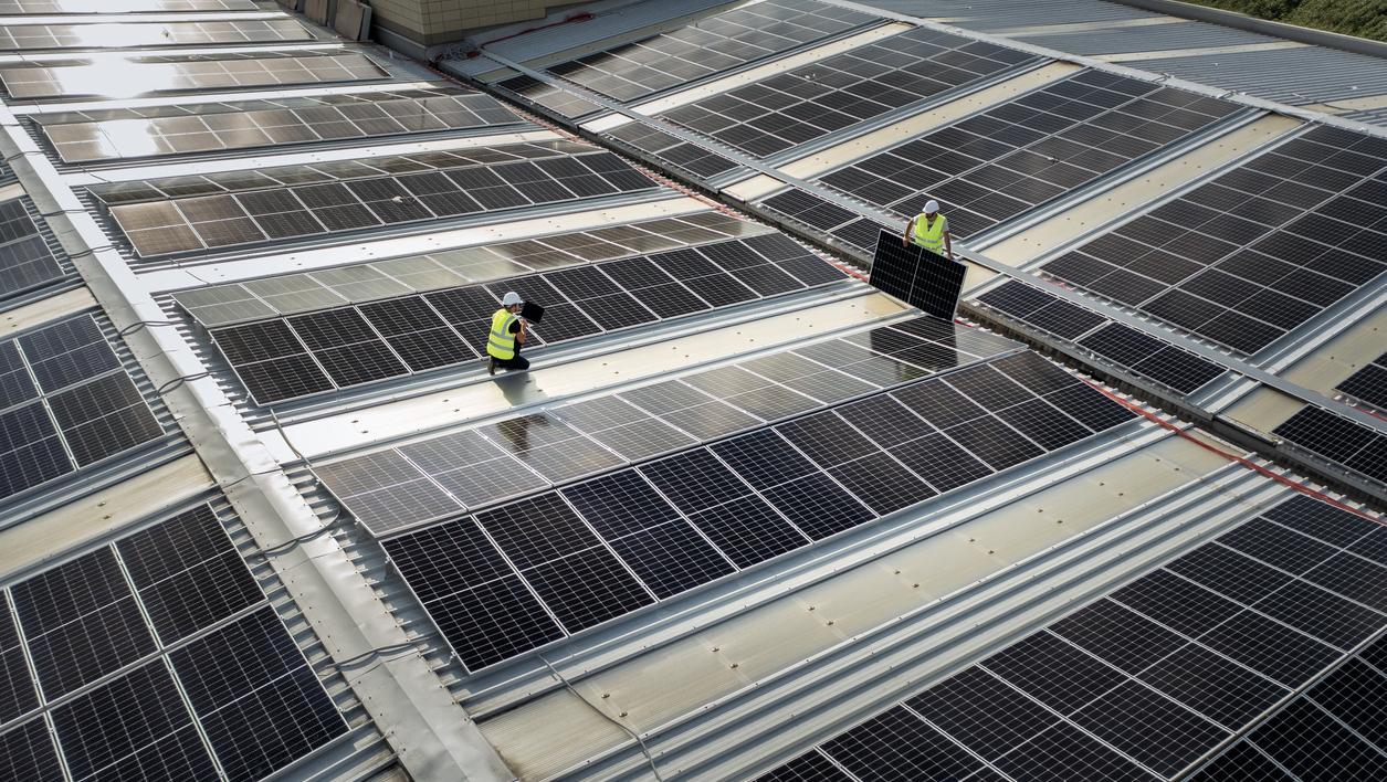 équipe d'ingénieurs utilisant la technologie lors de l'installation de panneaux solaires sur le toit d'un entrepôt