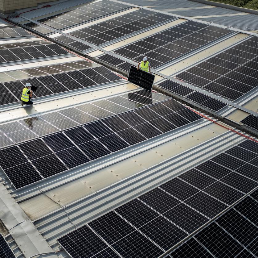 team of engineers using technology while installing solar panels on a roof of warehouse