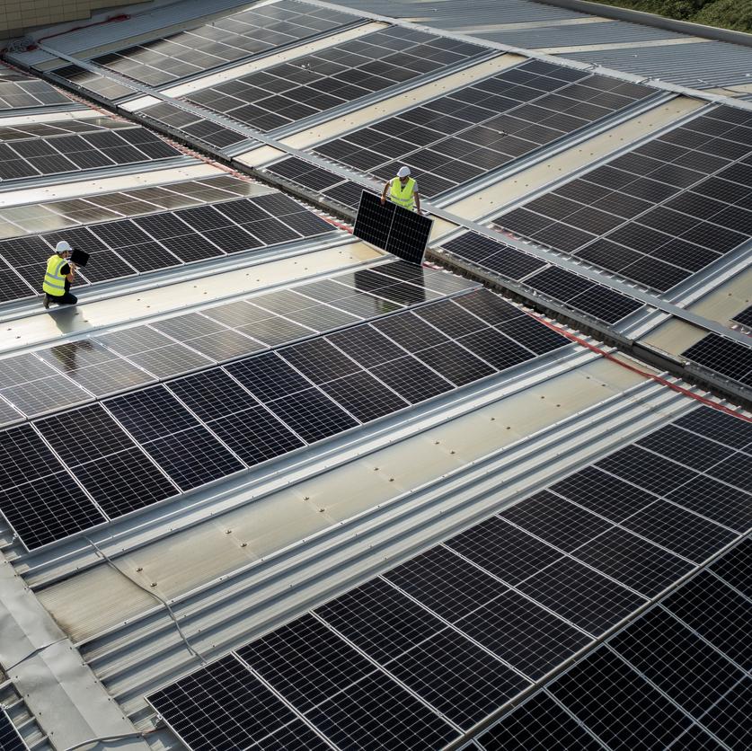 équipe d'ingénieurs utilisant la technologie lors de l'installation de panneaux solaires sur le toit d'un entrepôt
